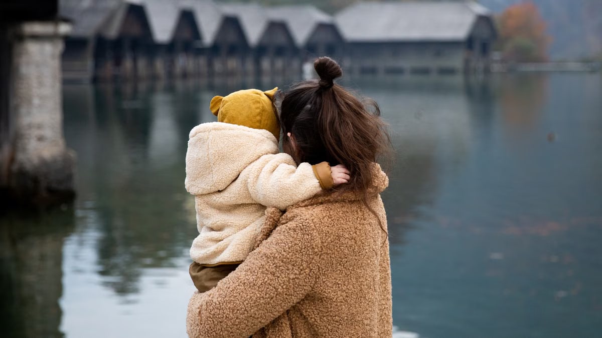 A mother and child embrace by a serene lake, showcasing love and togetherness in nature.
